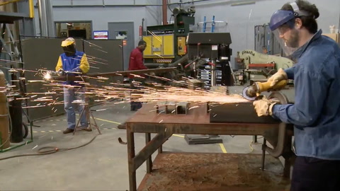Screen shot of video with man using hand grinder with sparks flying, wearing gloves and a face shield