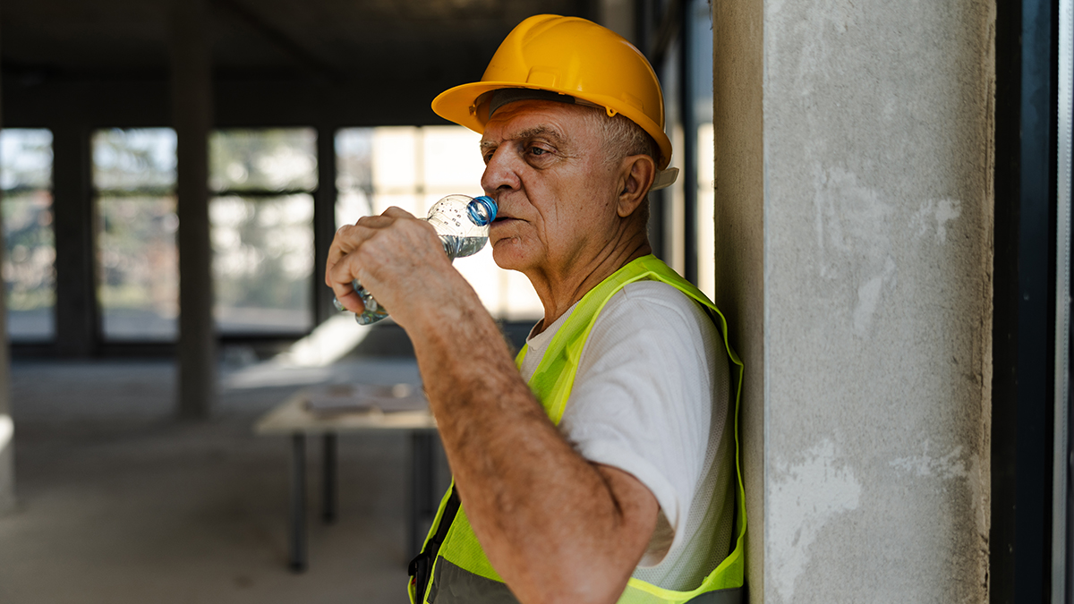 Older worker in a high visability vest and hard hat taking a break to drink water.
