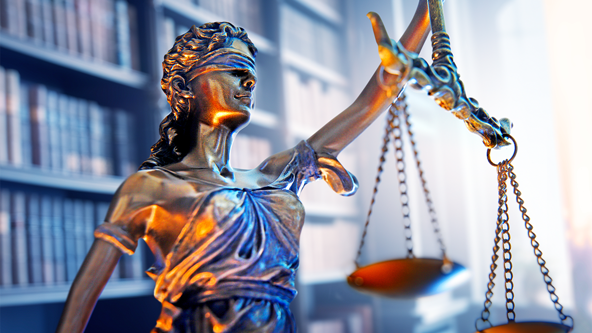 Statue of the Lady of Justice in front of a bookshelf.