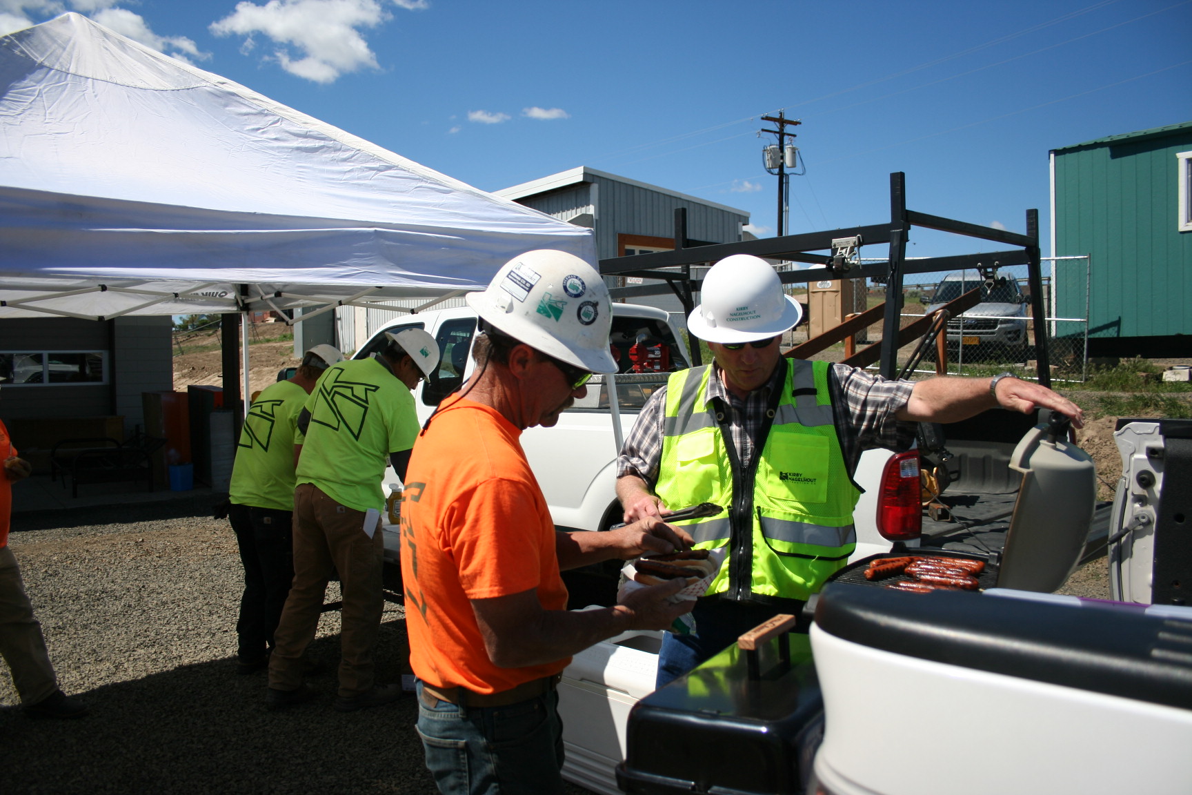 Men in hard hats and safety vests standing next to a barbeque on a truck tailgate