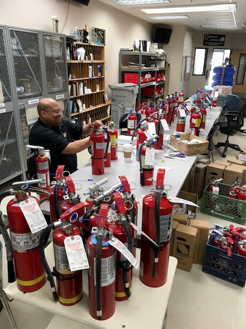 Photo of Comcast employee with a table full of fire extinguishers to test